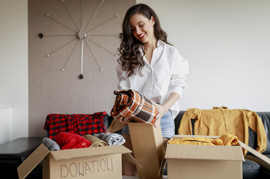 A smiling woman, holding a folded blanket. Two cardboard boxes are in front of her, one labeled "Donation"
